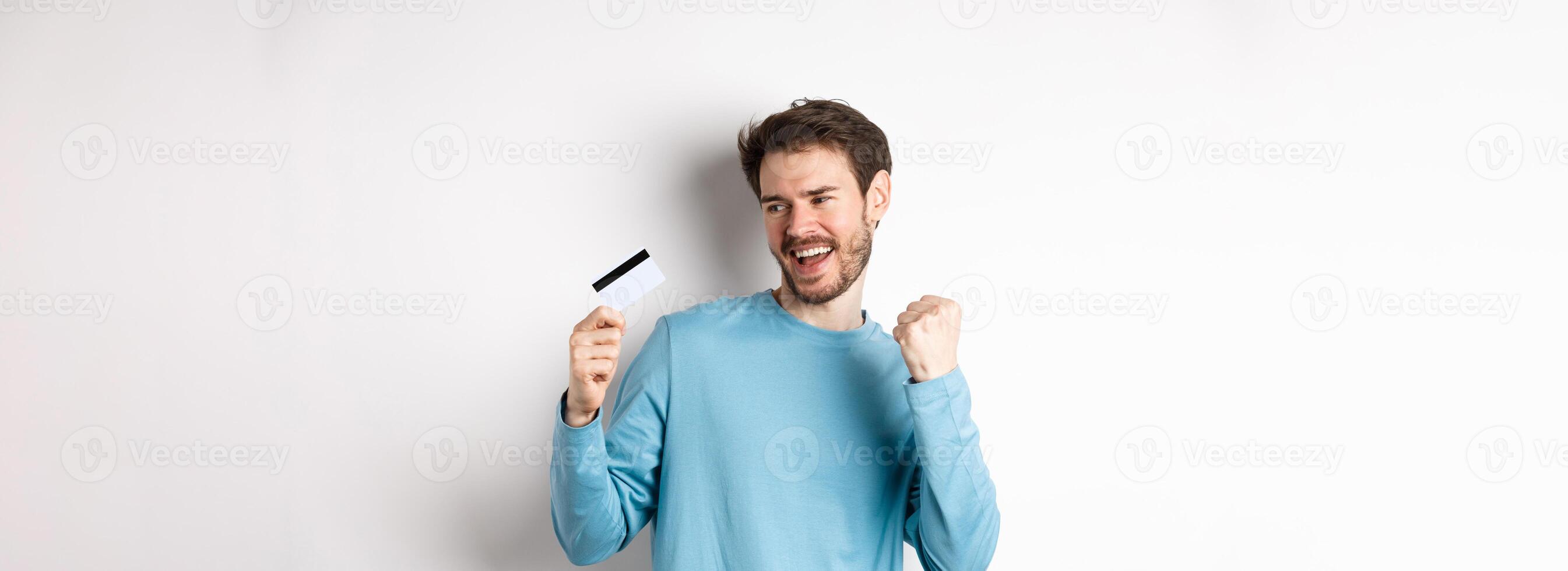 Happy man dancing with plastic credit card, smiling and saying yes, celebrating on white background photo