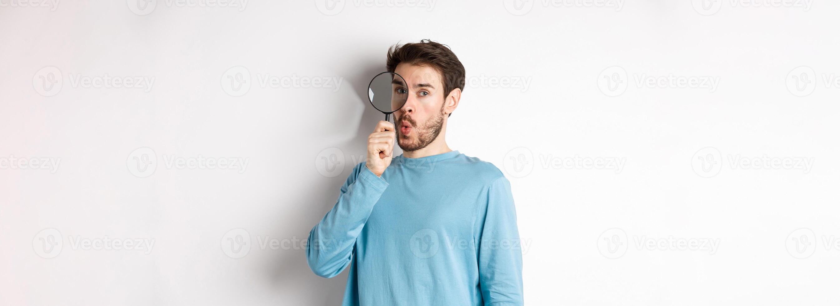 Surprised man found something, looking through magnifying glass with amazed face, standing over white background photo
