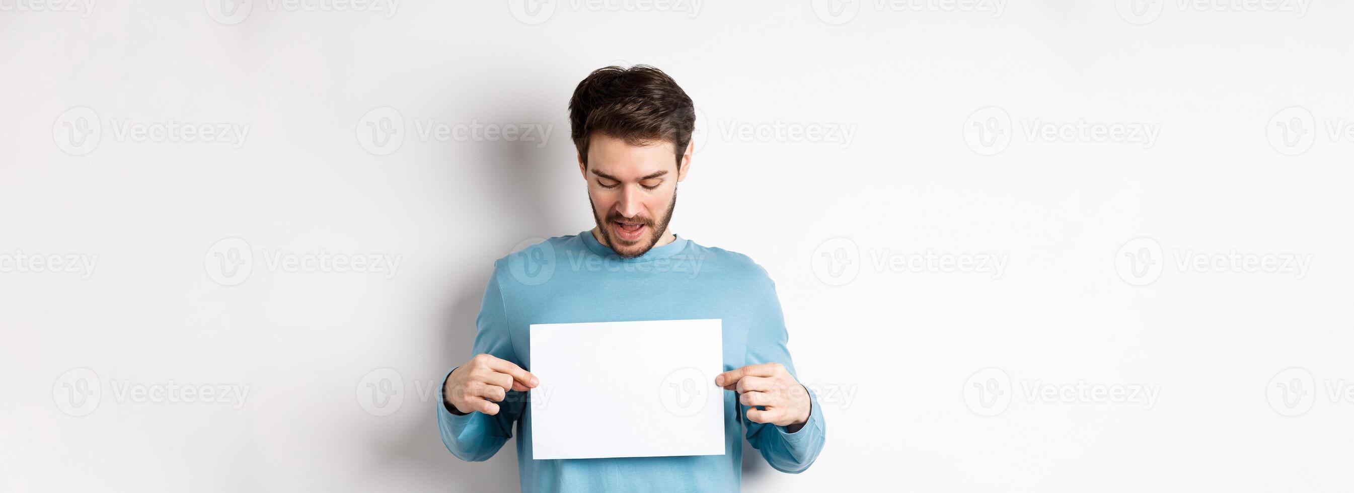 Excited bearded guy reading banner on blank piece of paper, showing logo, standing over white background photo