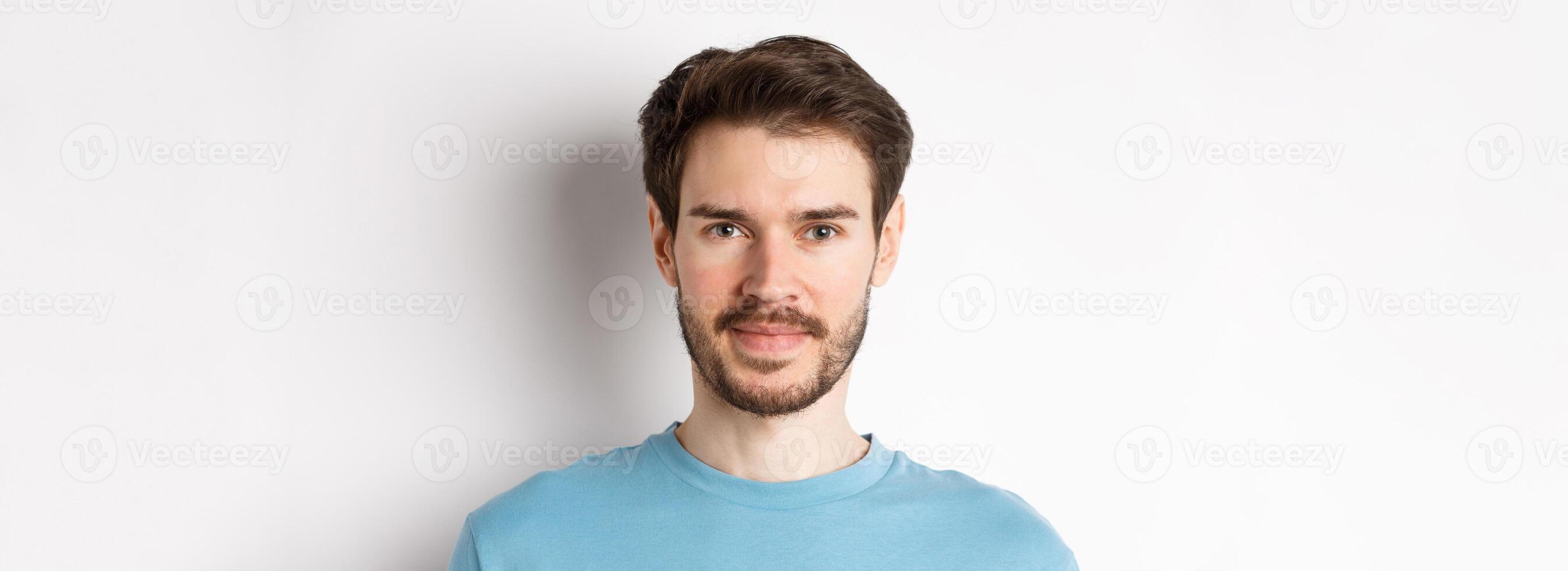 Close up of young handsome man with beard, smiling at camera with confidence, standing over white background photo