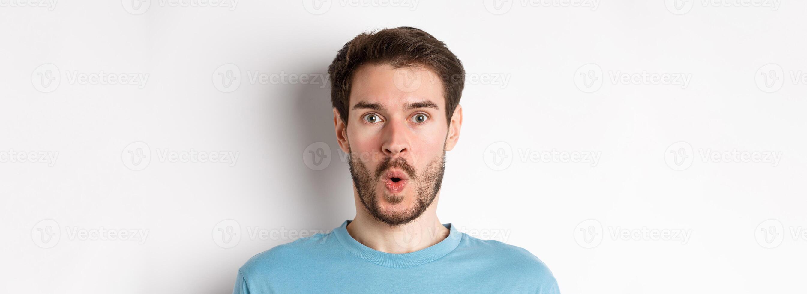 Close-up of surprised man face, saying wow and staring at camera amazed, standing on white background photo