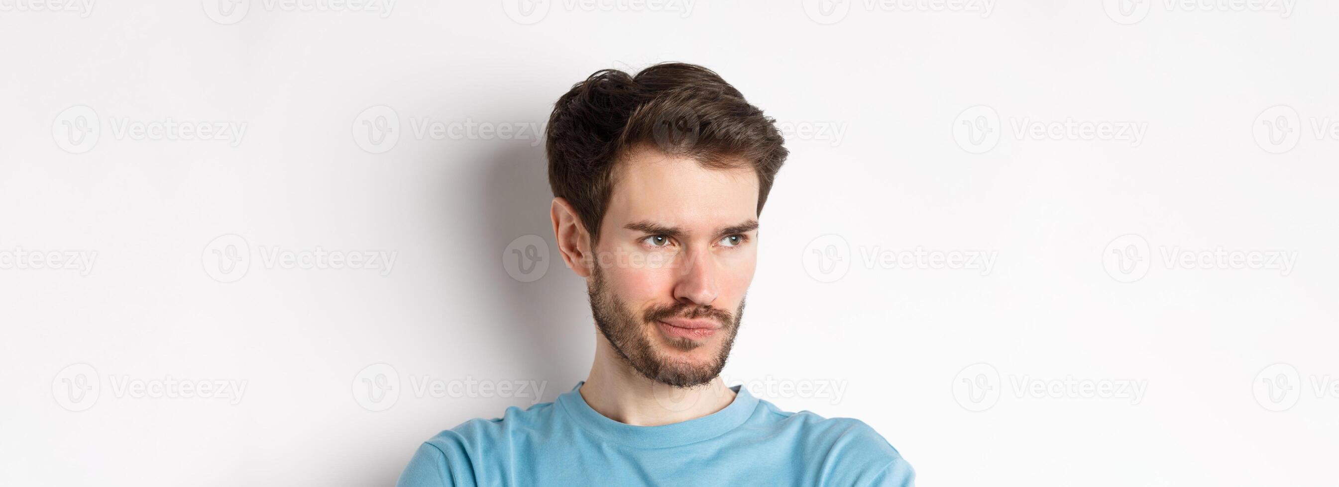 Close-up of disappointed bearded man, sulking and looking left with pensive face, standing upset over white background photo