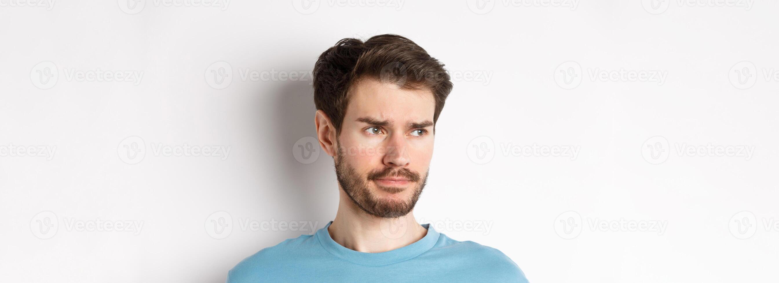 Close-up of disappointed sad man, grimacing and frowning, looking left upset, standing doubtful against white background photo