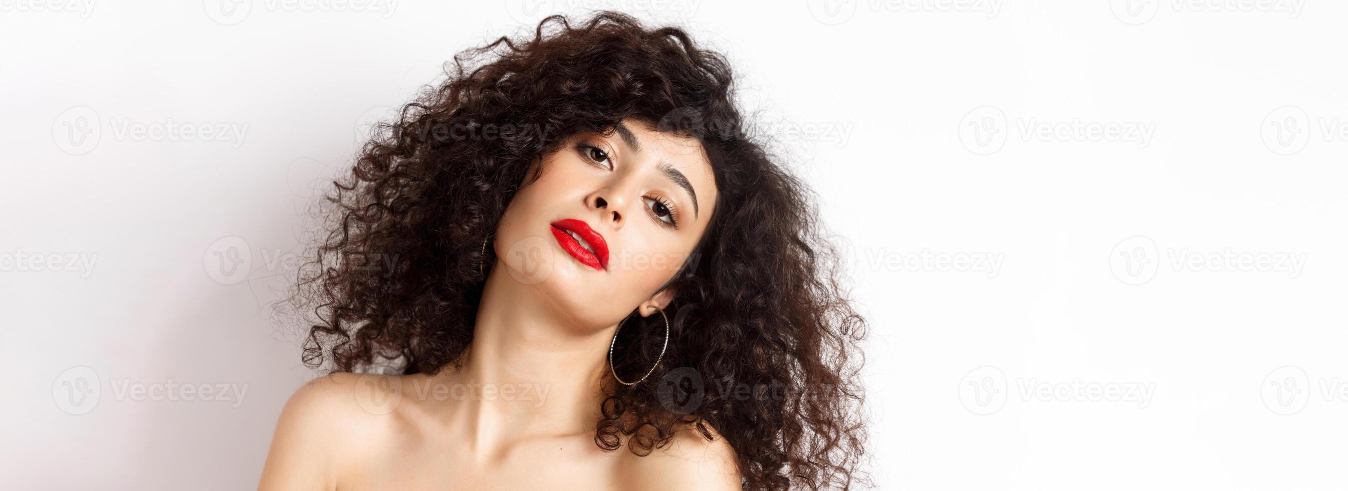Close-up portrait of sensual and romantic woman with curly hair, red lips, looking seductive at camera, posing on white background photo