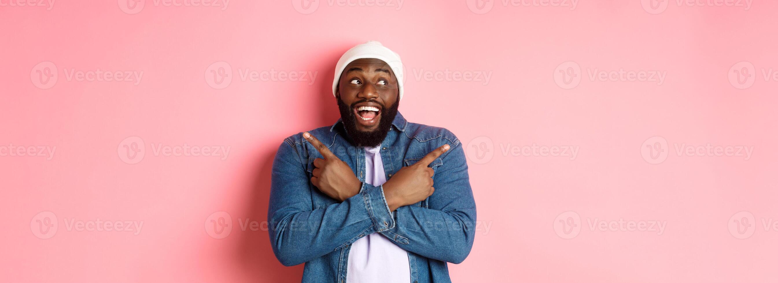 Excited young african-american man pointing sideways, showing two choices and making decision, smiling happy, standing over pink background photo