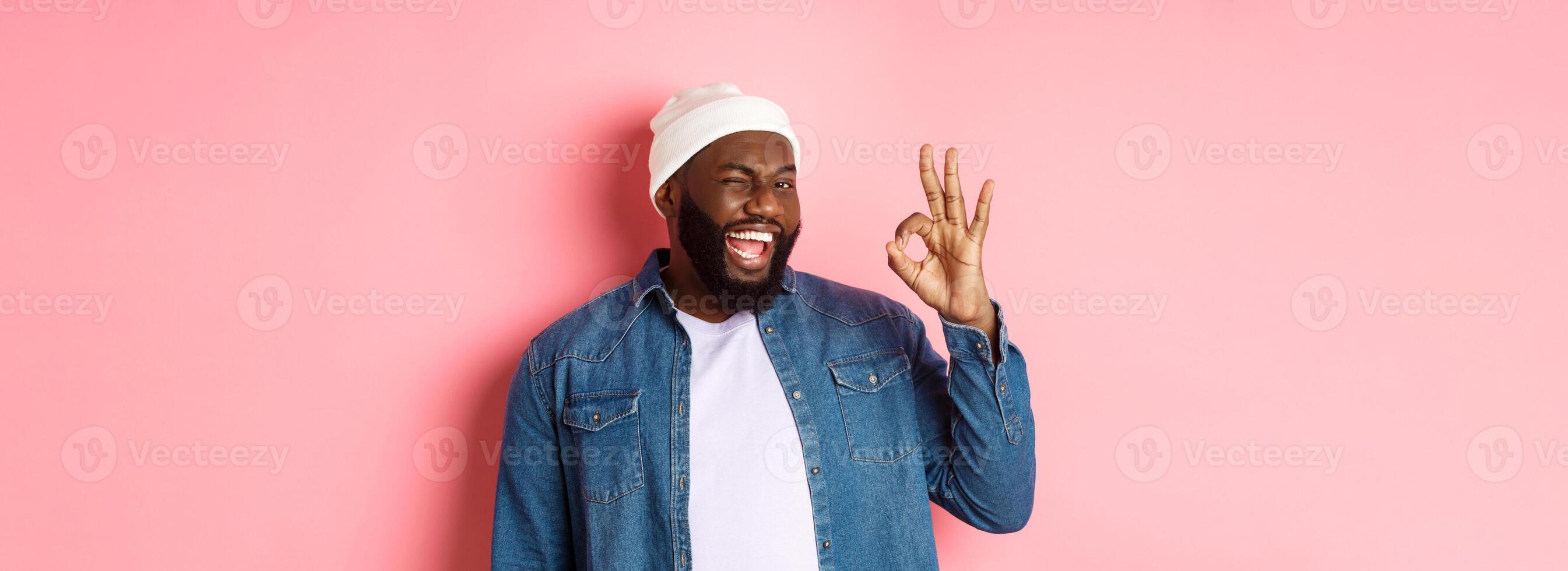 Happy smiling african american man showing okay sign, approve and praise good offer, standing over pink background photo