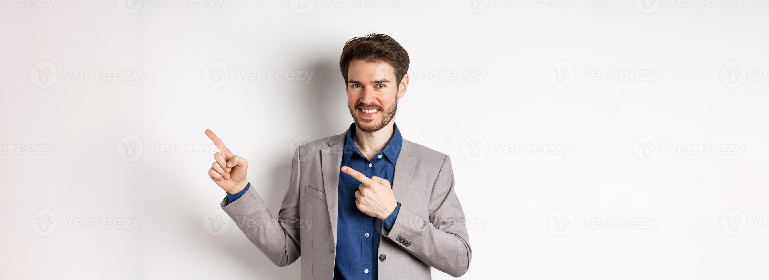 Handsome smiling man in business suit pointing fingers at upper right corner, showing logo, advertising company, standing on white background photo