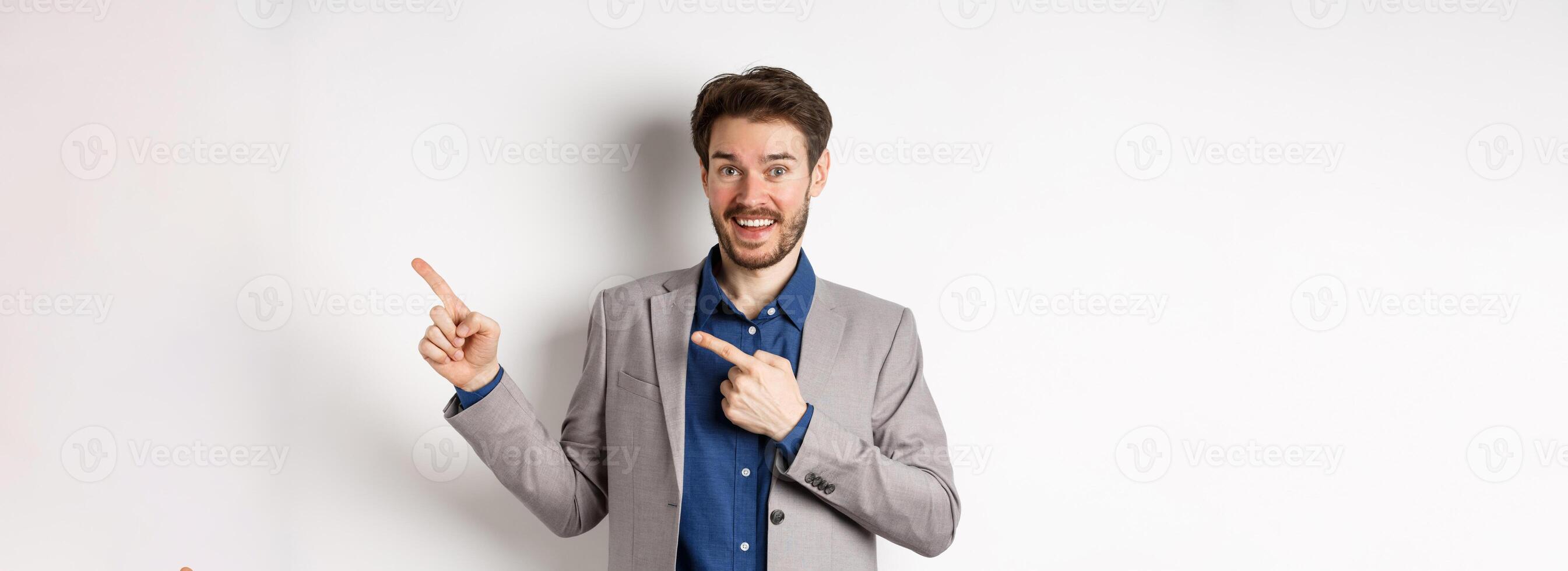 Happy businessman in suit pointing fingers right and smiling excited, showing special deal, standing on white background photo