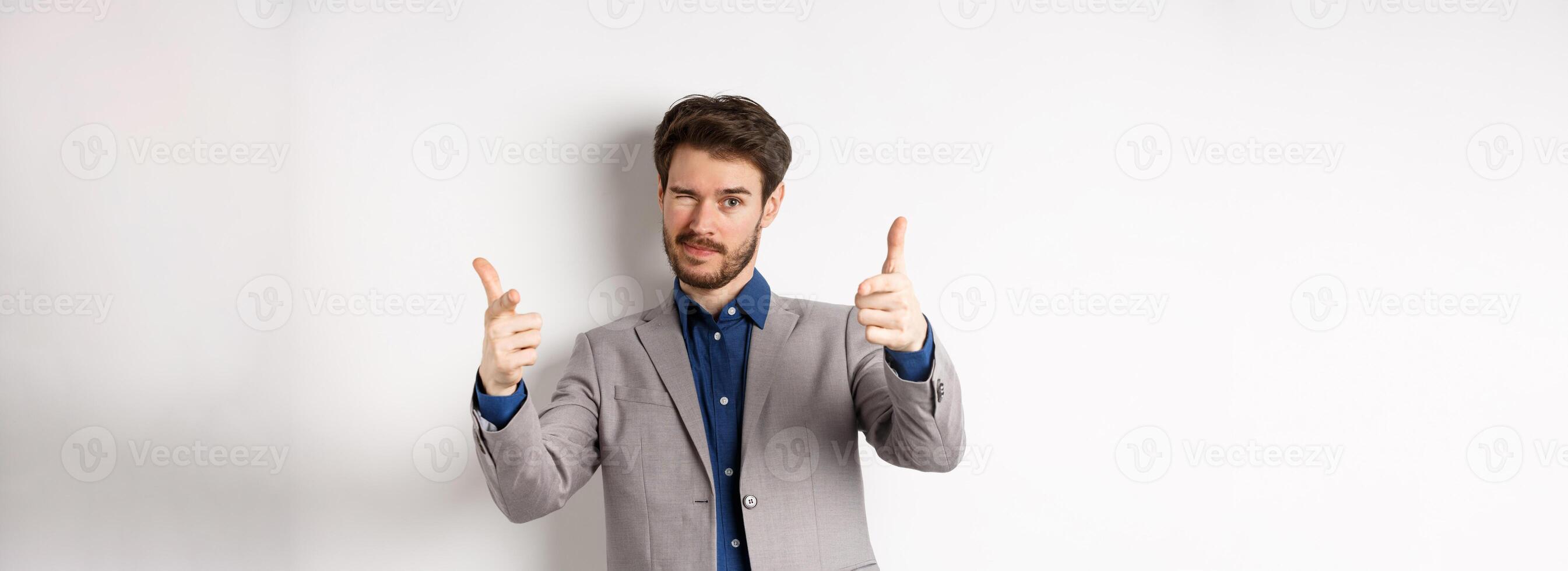 You got this. Handsome caucasian businessman in suit pointing fingers at camera and winking, motivating people, inviting to work in company, standing on white background photo