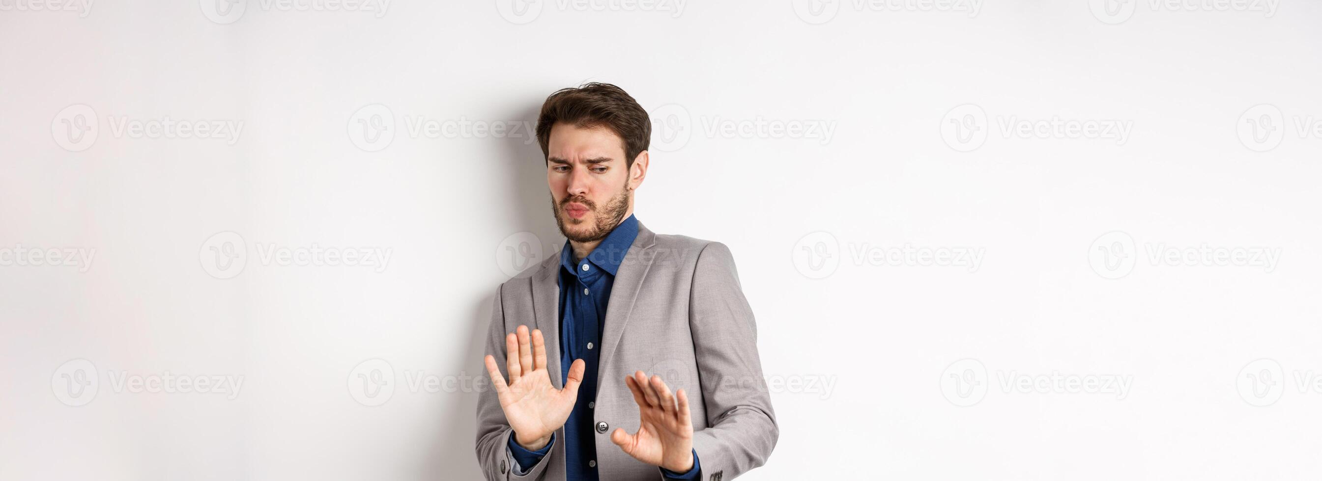 Stay away. Reluctant businessman step back with concerned disgusted face, raising hands to block bad offer, rejecting something awful, tilting from disgust, white background photo