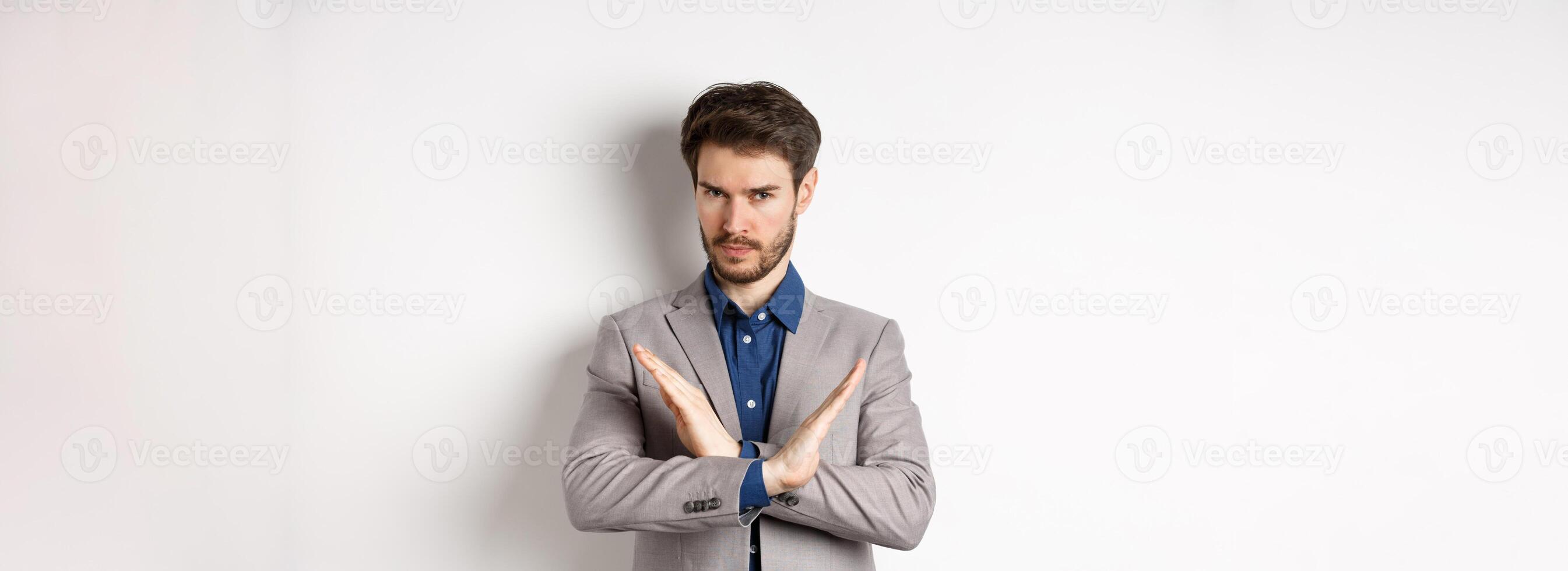Serious business man making cross and says no, looking determined, disagree and prohibit something bad, tell to stop, standing in suit on white background photo