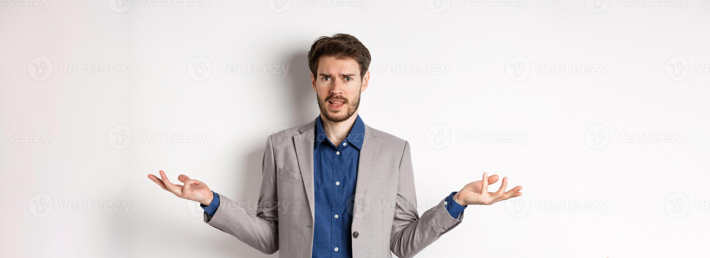 So what big deal. Confused and annoyed businessman spread hands sideways and frowning puzzled, cant understand whats wrong, standing on white background photo