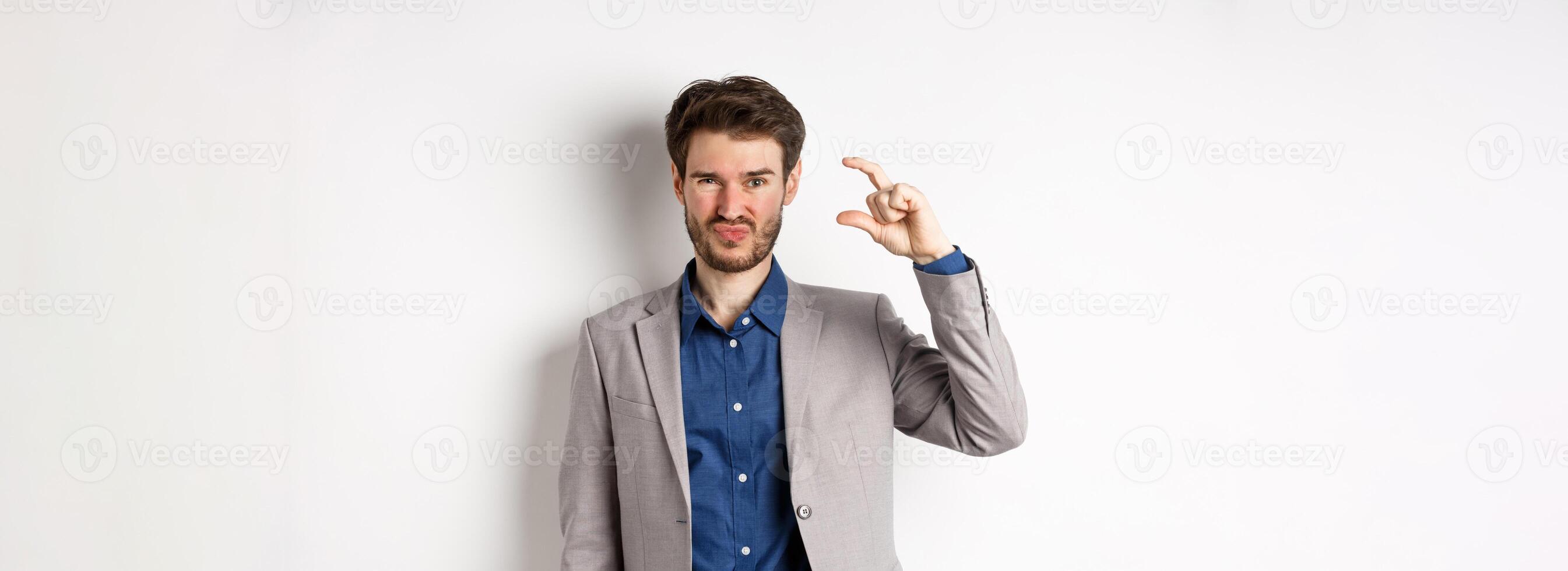 Disappointed businessman showing small size and grimacing upset, little income, standing displeased against white background photo