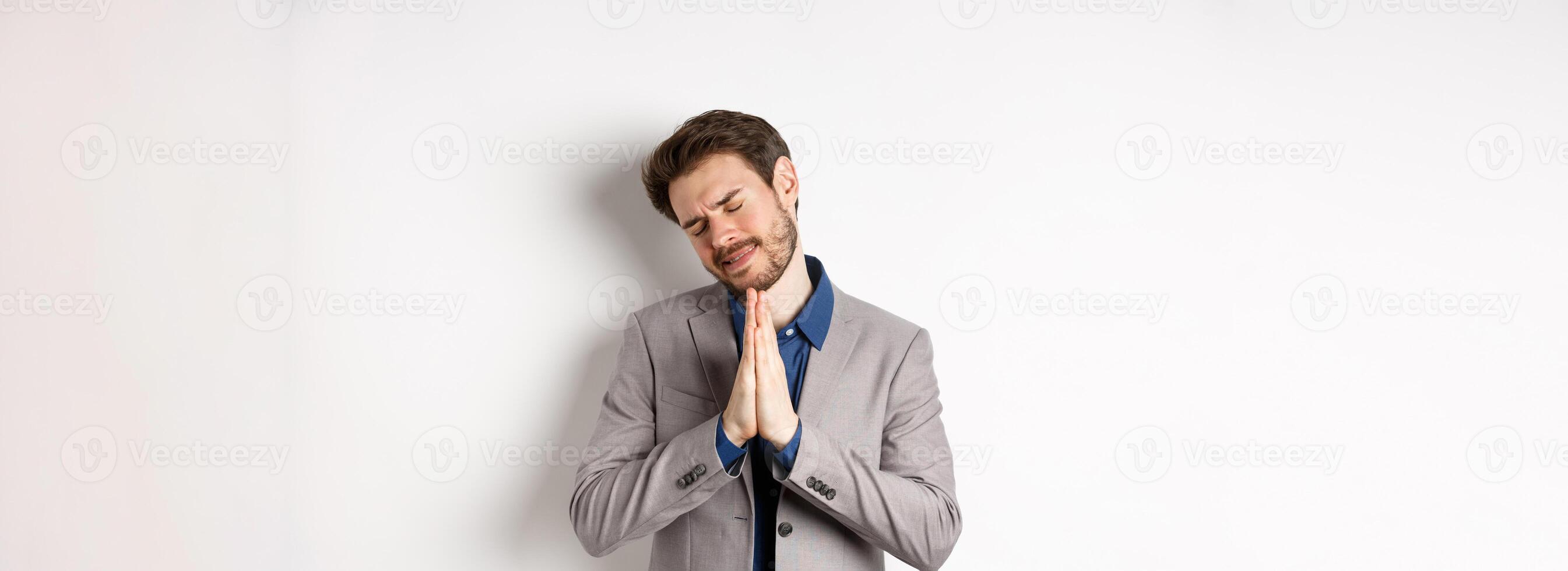 Pleading businessman begging for help, holding hands in pray and asking for favour, need something, say please, standing on white background photo
