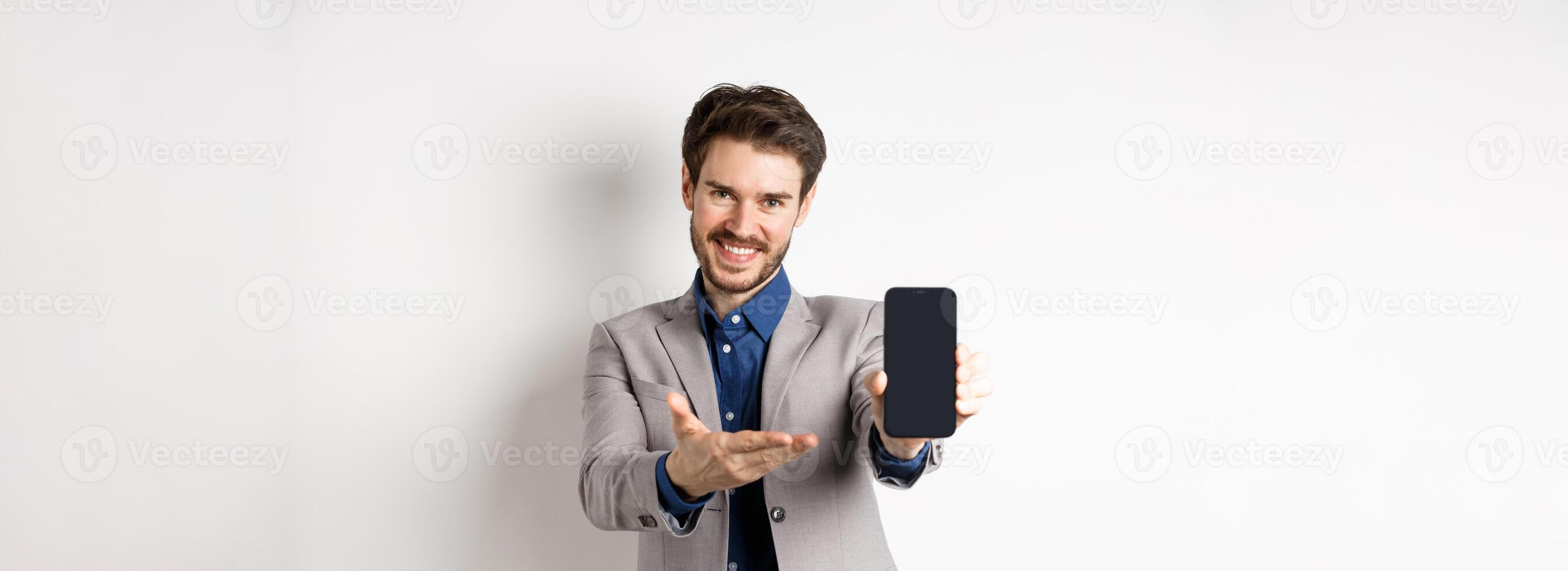 E-commerce and online shopping concept. Here you go. Smiling pleasant salesman demonstrate promo on phone, showing empty smartphone screen, white background photo