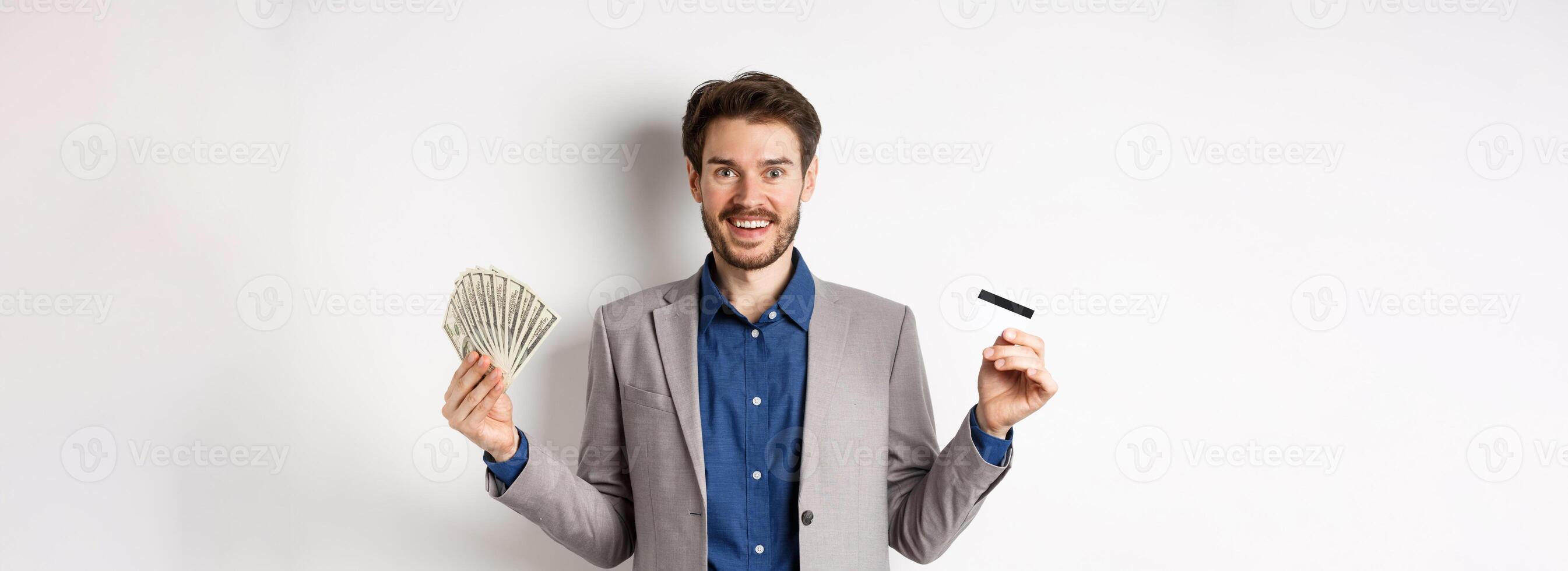 Happy successful businessman in suit showing money and credit card, smiling at camera, white background photo