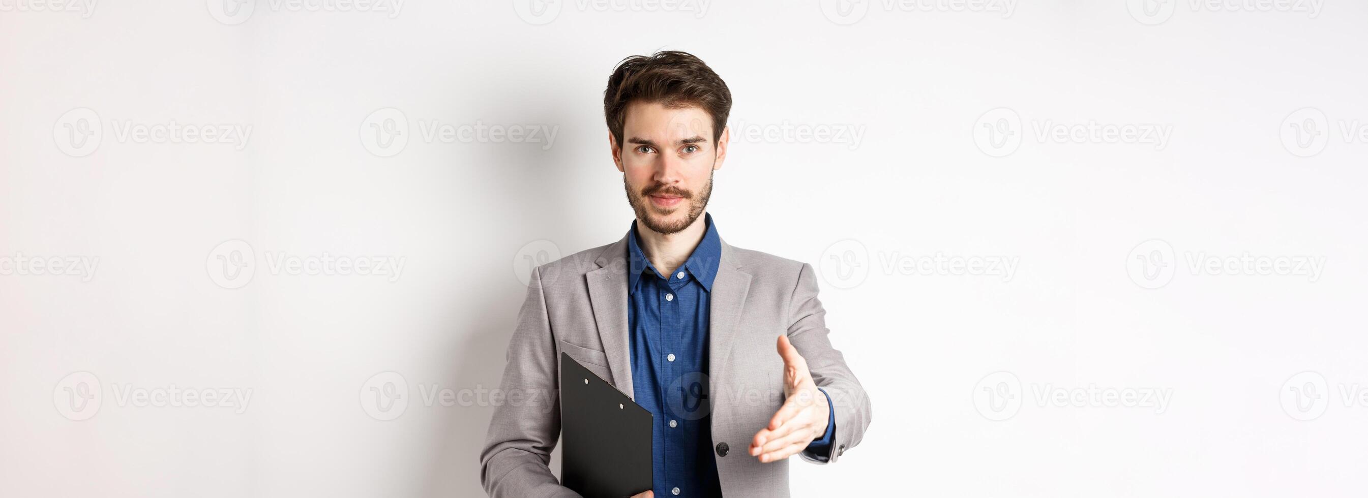 Confident businessman with clipboard giving hand for handshake, greeting business partners on meeting, standing on white background in suit photo