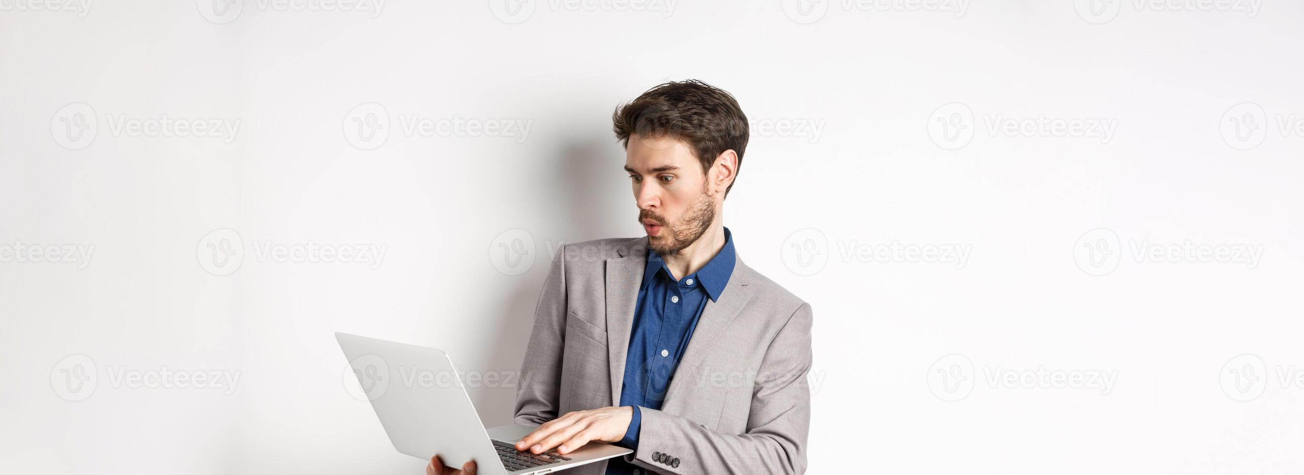 Excited salesman looking at laptop screen amazed, tilt away from excitement, checking out news in network, standing against white background photo