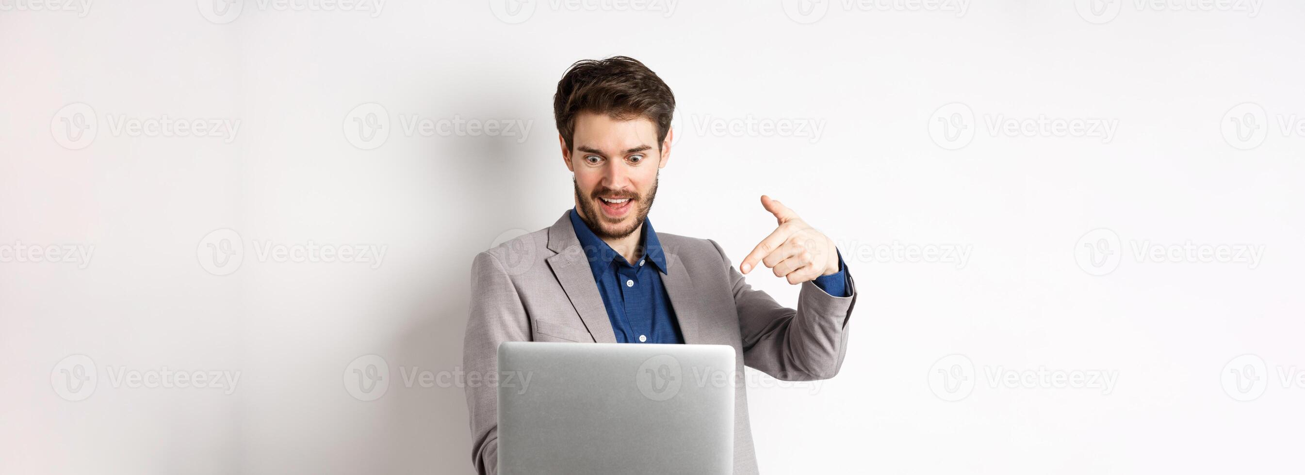 Excited male ceo manager looking and pointing at laptop with amazed smile, checking out special deal online, standing on white background photo