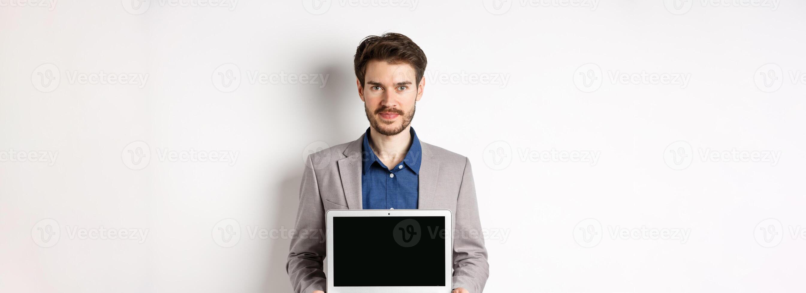 Handsome caucasian businessman in suit showing empty laptop screen, demonstrate promo, standing on white background photo