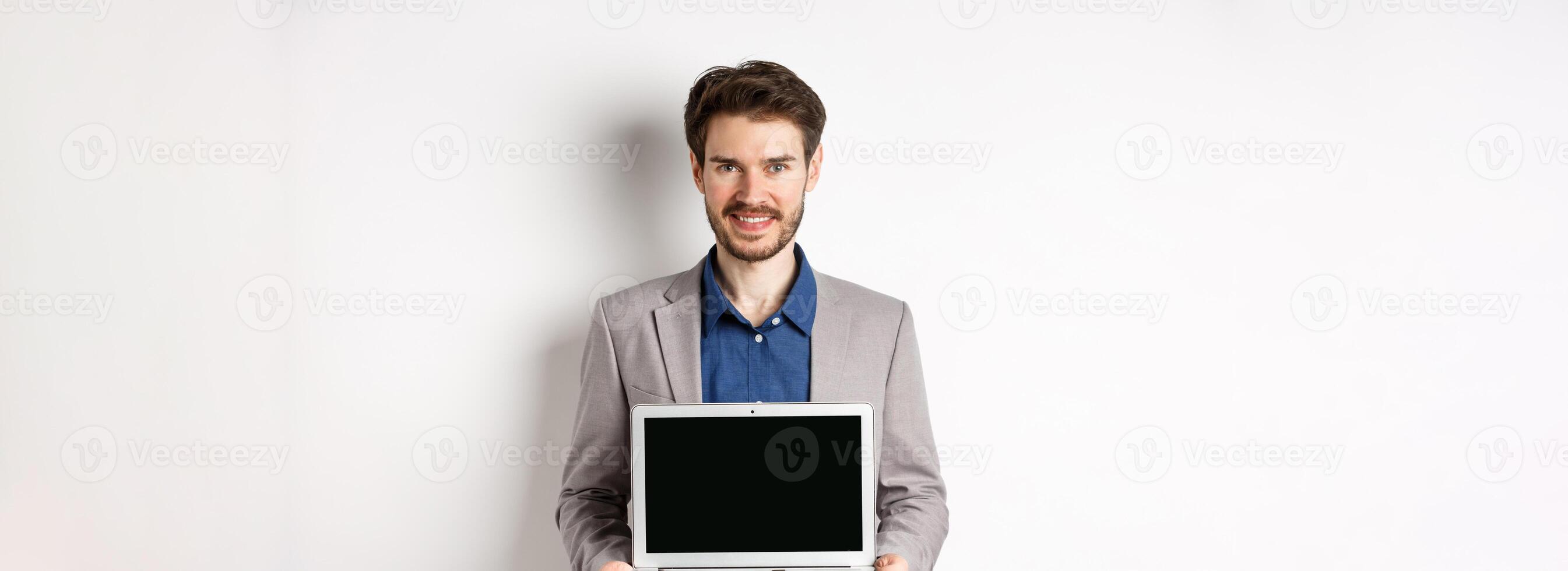 Handsome caucasian businessman in suit showing empty laptop screen, demonstrate promo, standing on white background photo