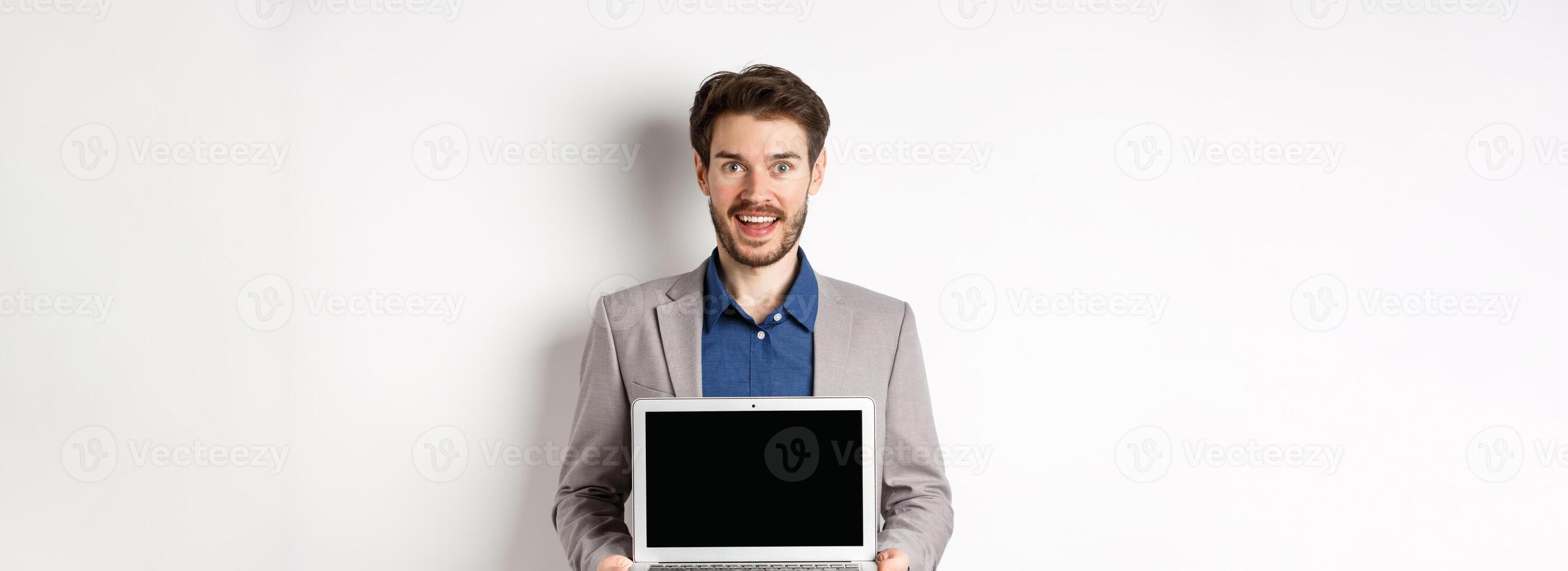 Handsome caucasian businessman in suit showing empty laptop screen, demonstrate promo, standing on white background photo