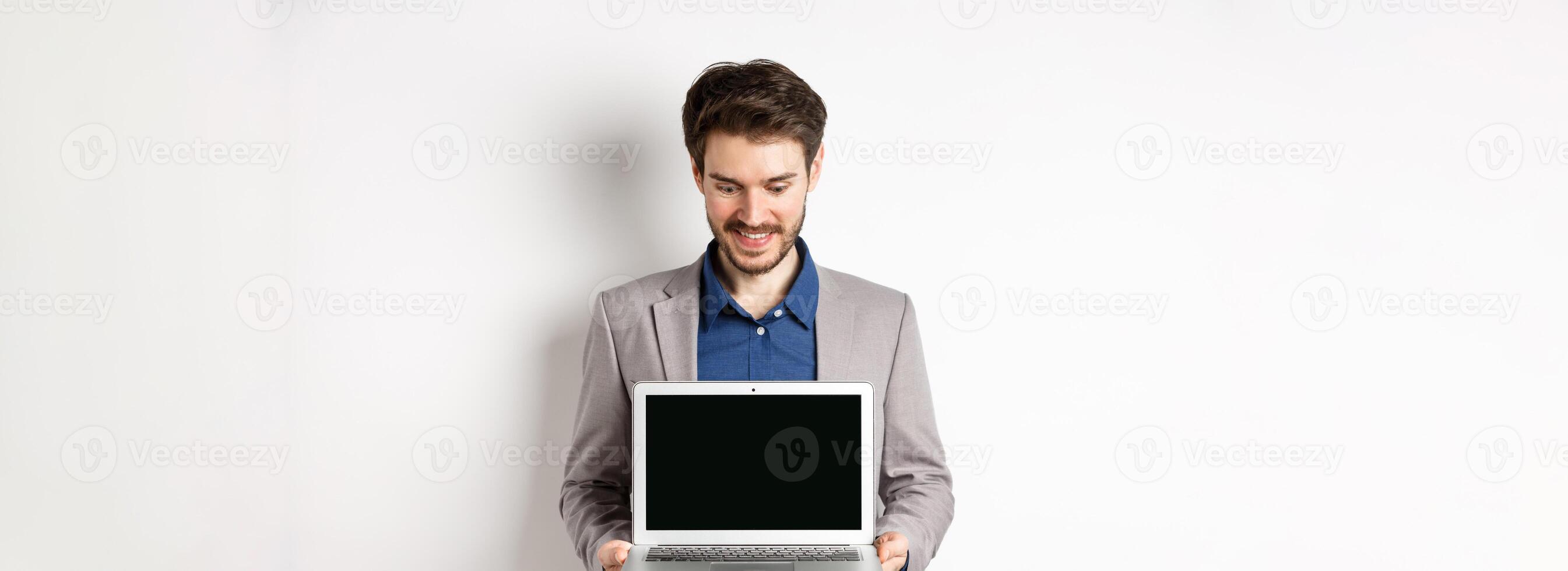 Handsome caucasian businessman in suit showing empty laptop screen, demonstrate promo, standing on white background photo