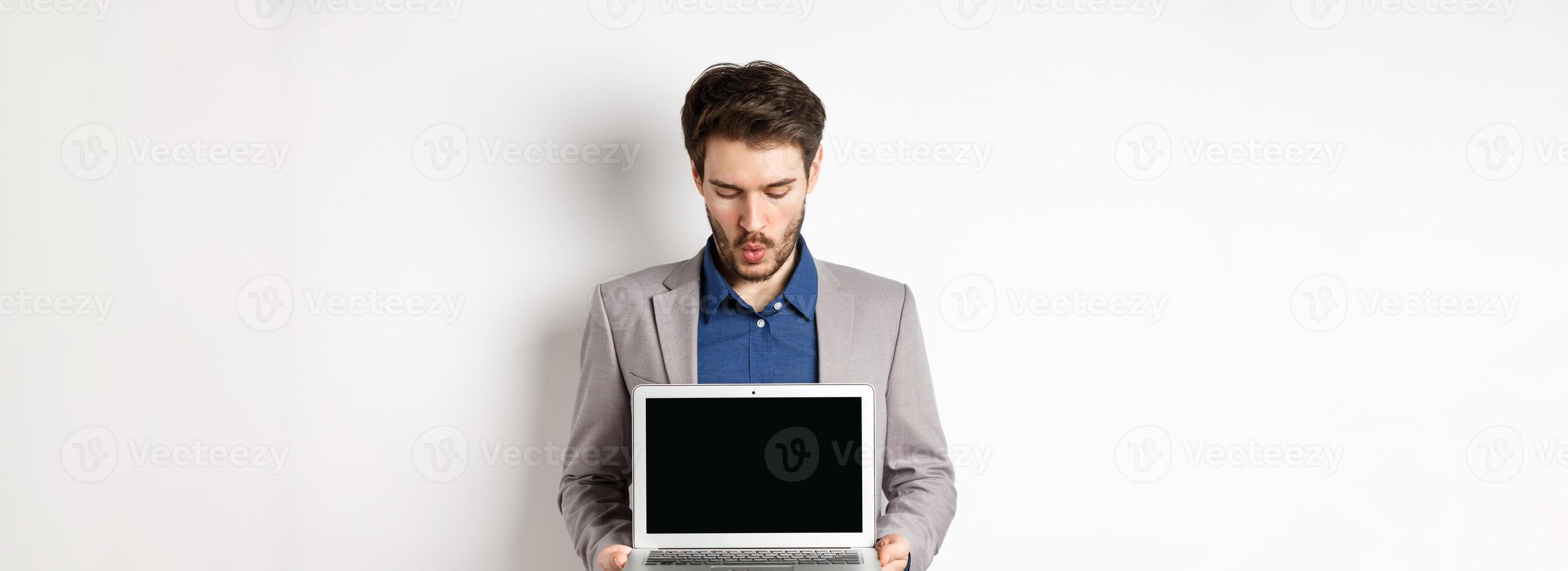 Handsome caucasian businessman in suit showing empty laptop screen, demonstrate promo, standing on white background photo