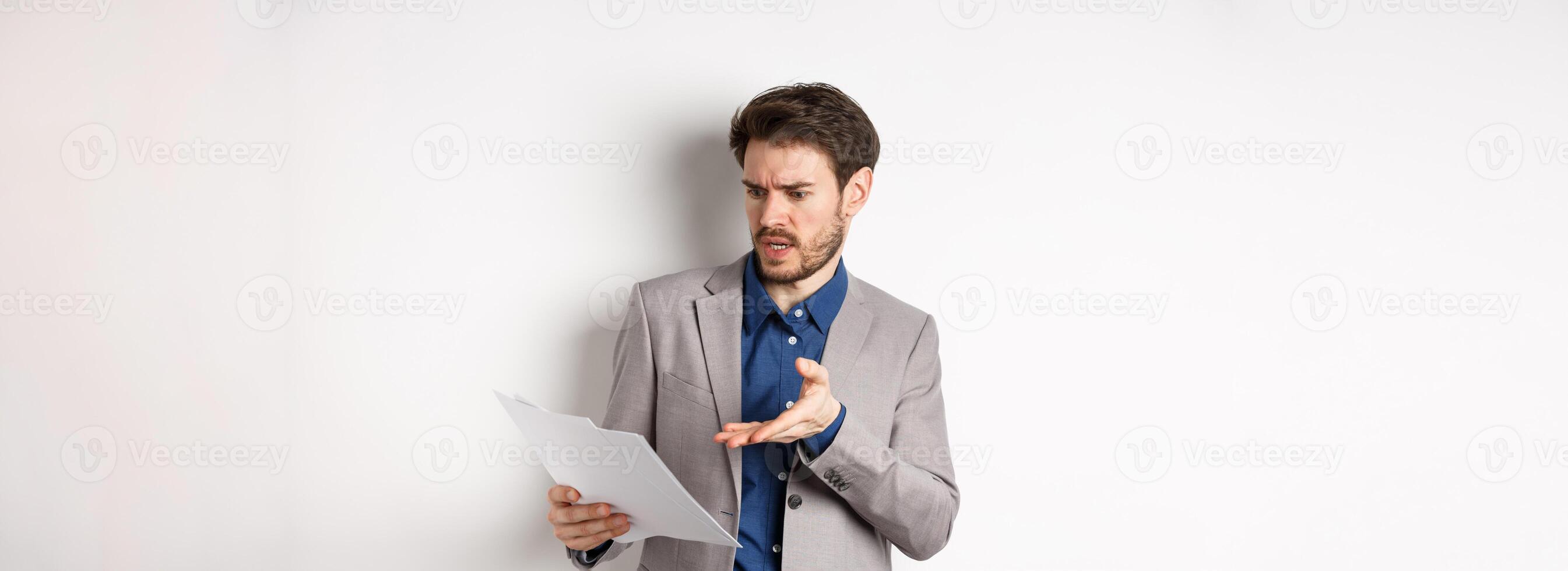 Angry employer looking at bad document, complaining on deal, pointing at paper frustrated, standing in suit on white background photo