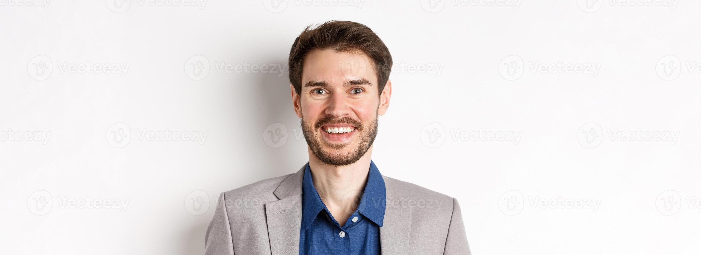 Close-up of happy bearded man in suit laughing and smiling, standing on white background photo