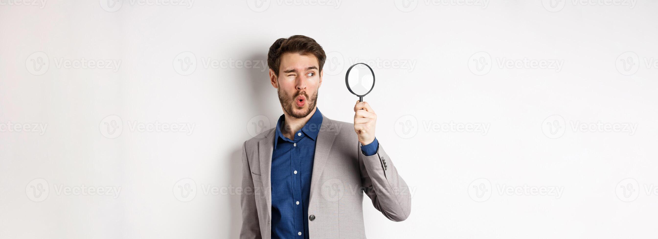 Excited funny guy in suit look through magnifying glass aside, checking out awesome thing, found something, white background photo