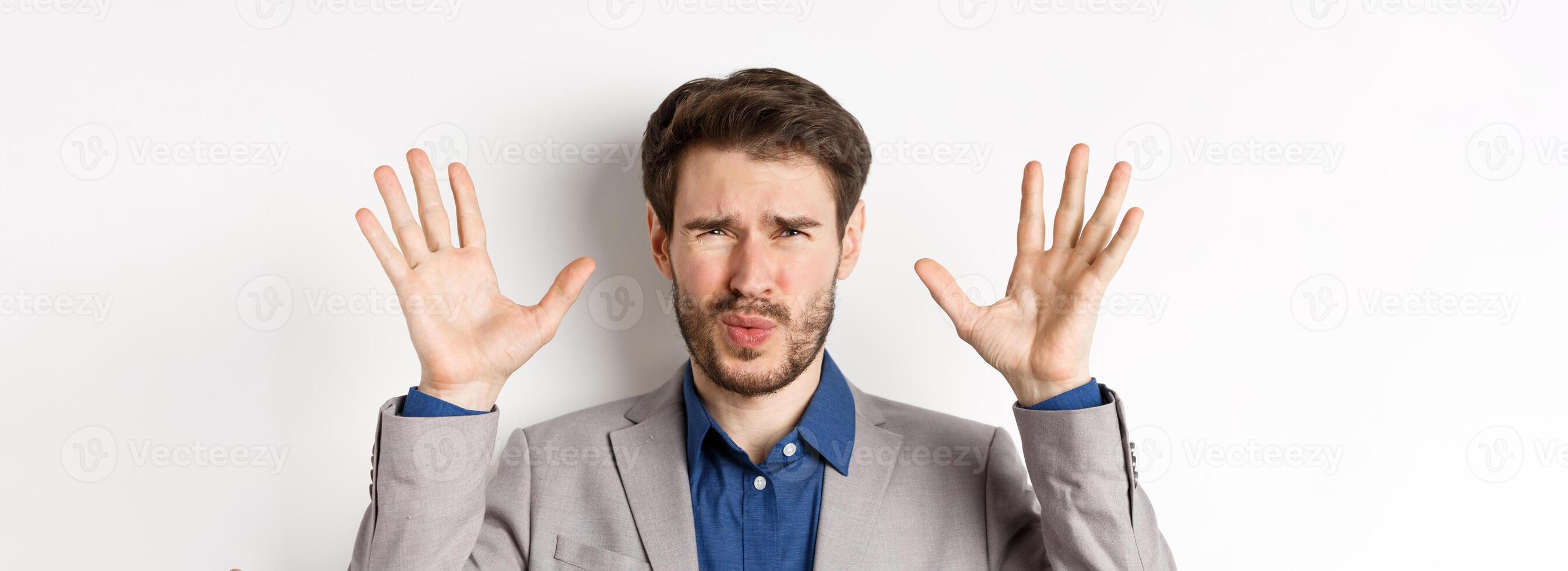 Close-up of disappointed and disgusted businessman raising hands up, grimacing from dislike and aversion, standing reluctant on white background photo