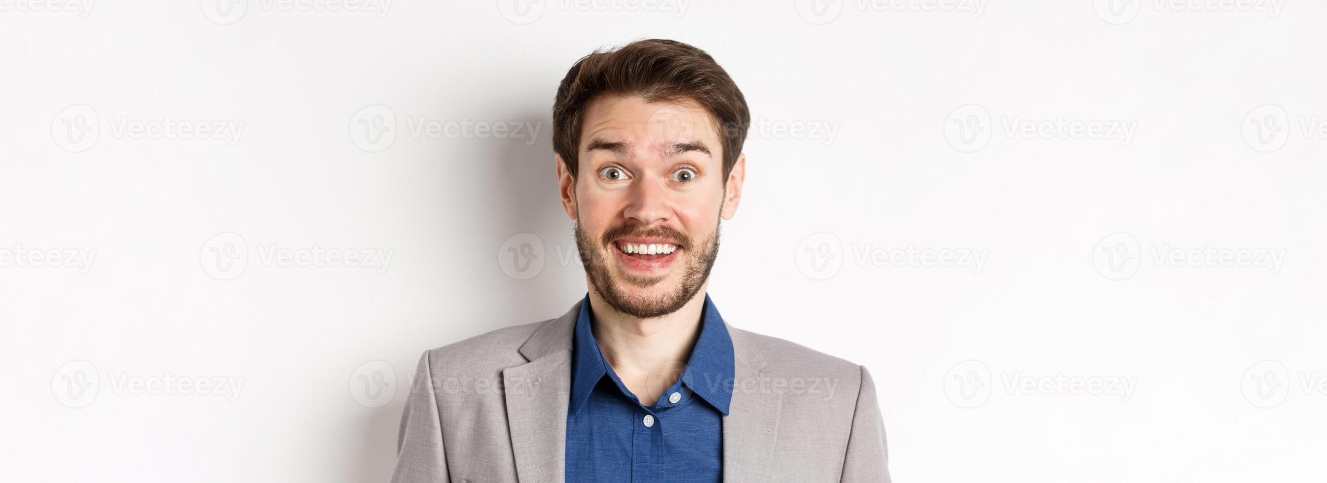 Close-up portrait of candid happy guy in suit looking excited at camera, smiling surprised, white background photo