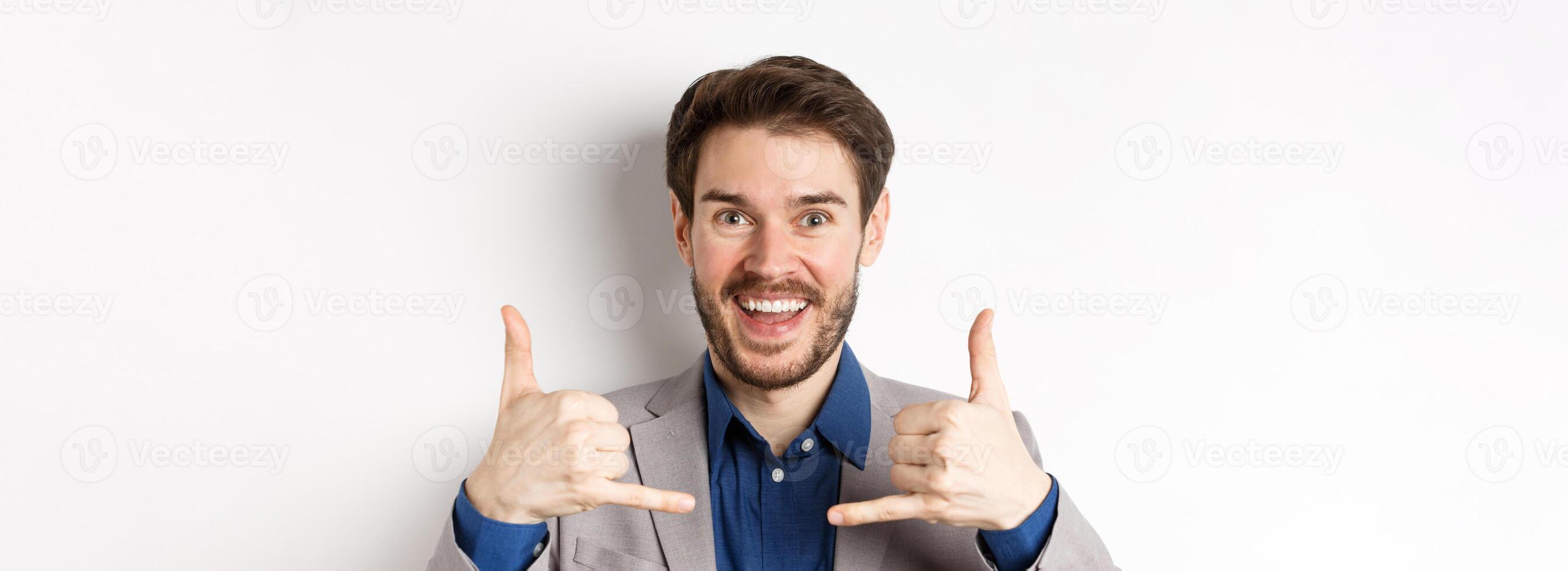 Excited salesman smiling, showing phone signs and asking to give him call, giving his number, standing on white background in suit photo
