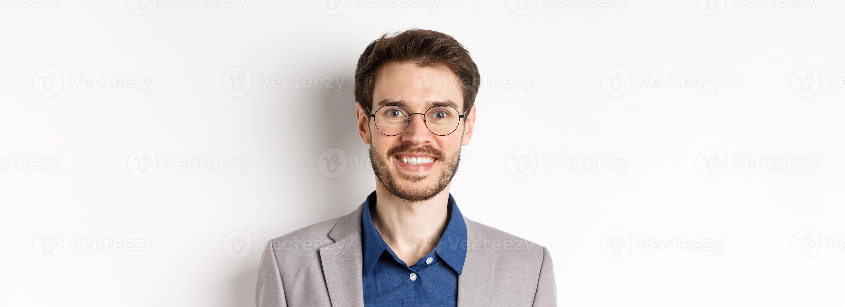 Close-up of handsome young office worker in glasses and suit smiling at camera, looking happy on white background photo