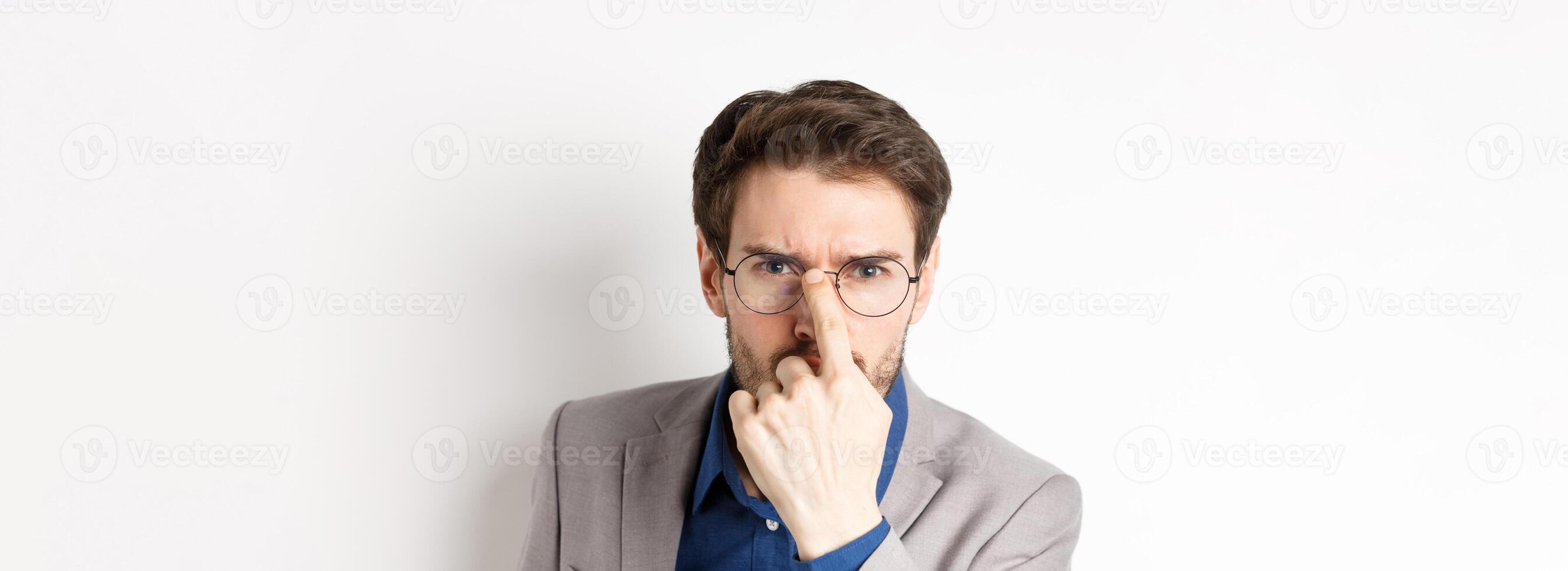 Serious boss in suit frowning, put on glasses and looking suspicious at camera, white background photo