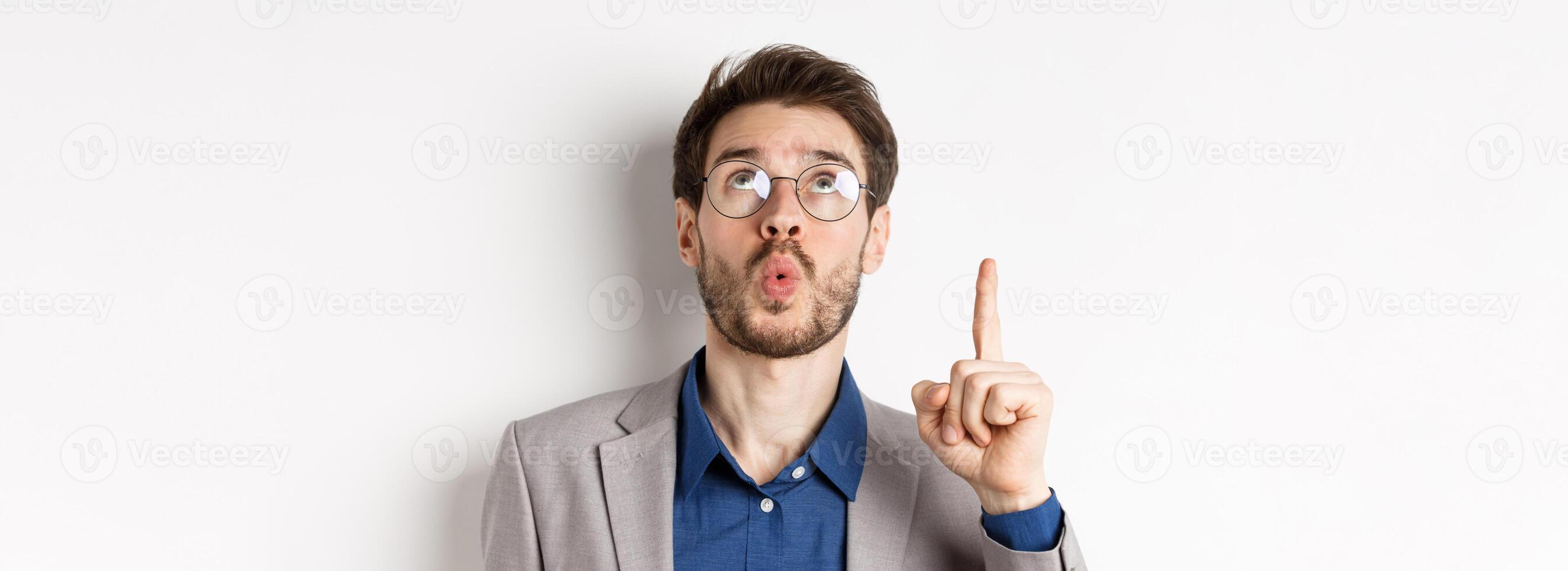 Excited handsome man in glasses and business suit, look up and pointing at top advertisement, exclaim wow with amazed expression, white background photo