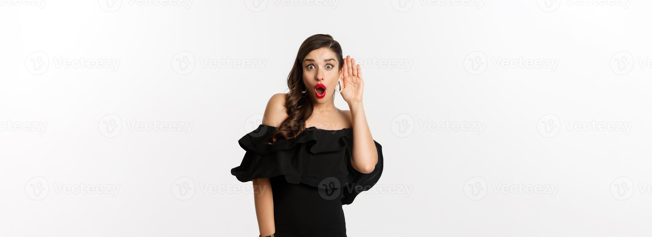 Fashion and beauty. Image of excited woman eavesdropping, holding hand near ear and leaning left to hear gossips, white background photo