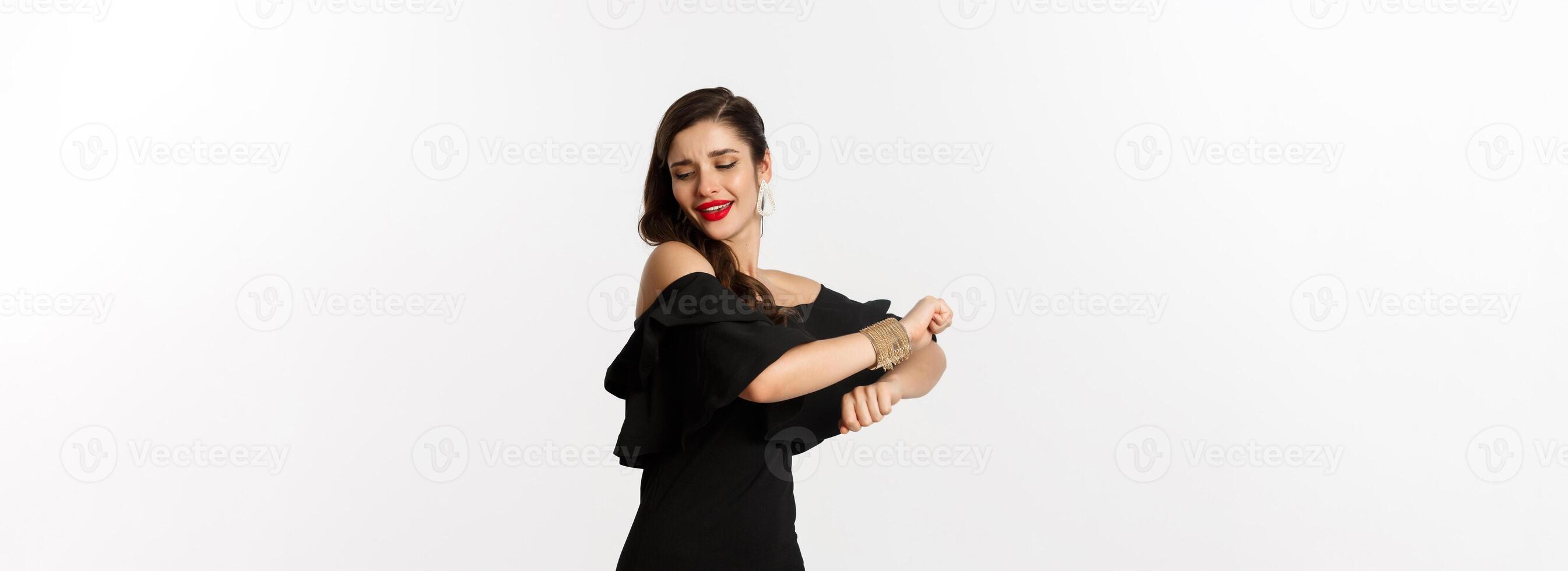 Fashion and beauty. Attractive woman feeling happy and dancing in black party dress, standing carefree against white background photo