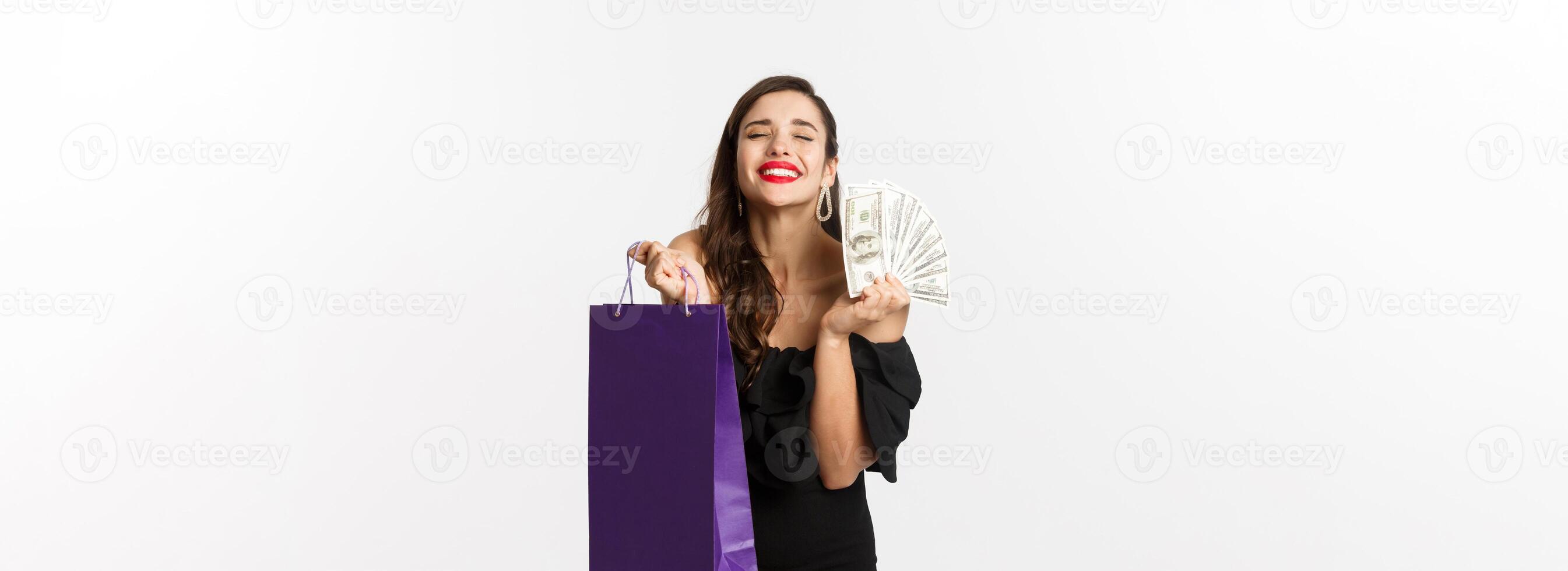Satisfied and happy woman enjoying shopping, holding bag and money, smiling pleased, standing over white background photo