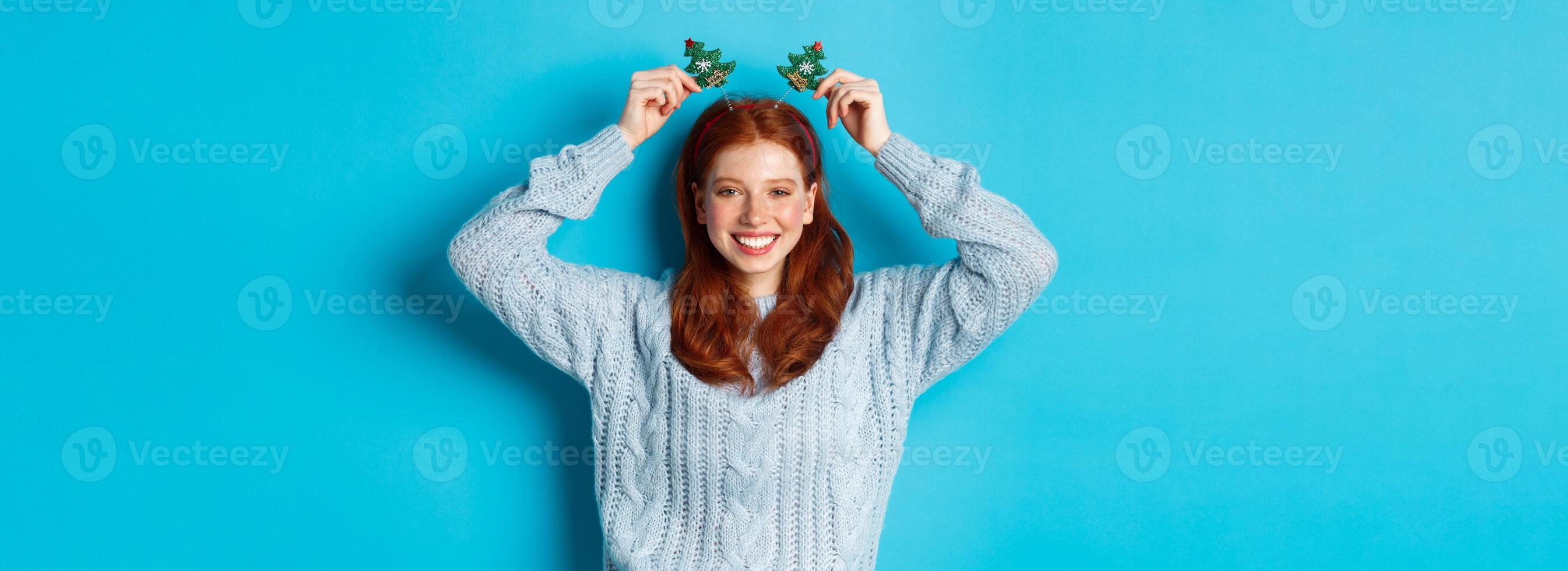 Winter holidays and Christmas sales concept. Beautiful redhead female model celebrating New Year, wearing funny party headband and sweater, smiling at camera photo