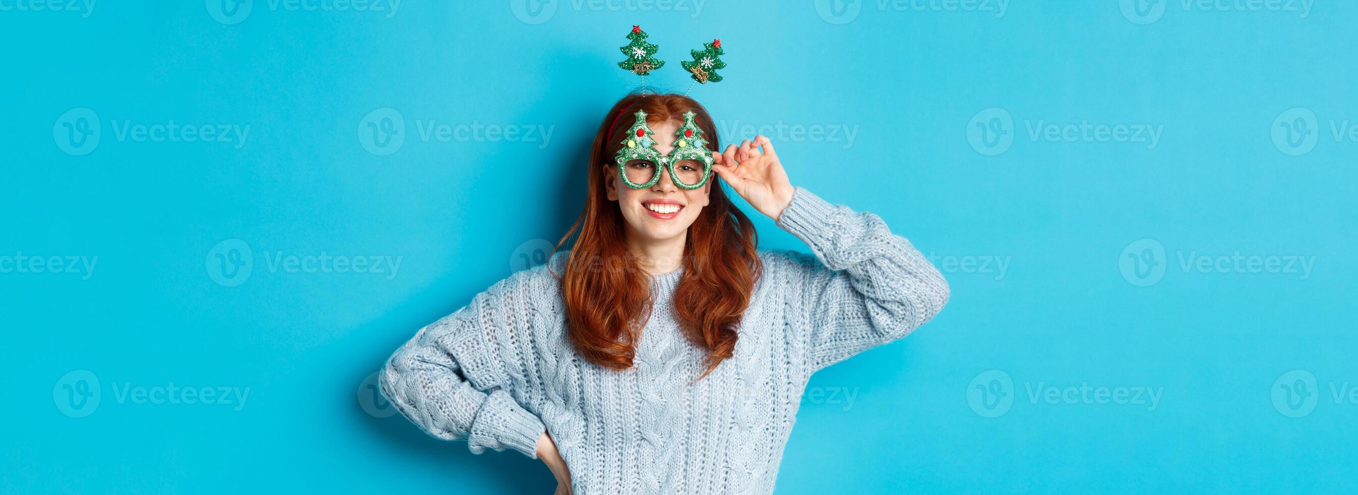 Winter holidays and Christmas sales concept. Beautiful redhead female model celebrating New Year, wearing funny party headband and glasses, smiling at camera photo