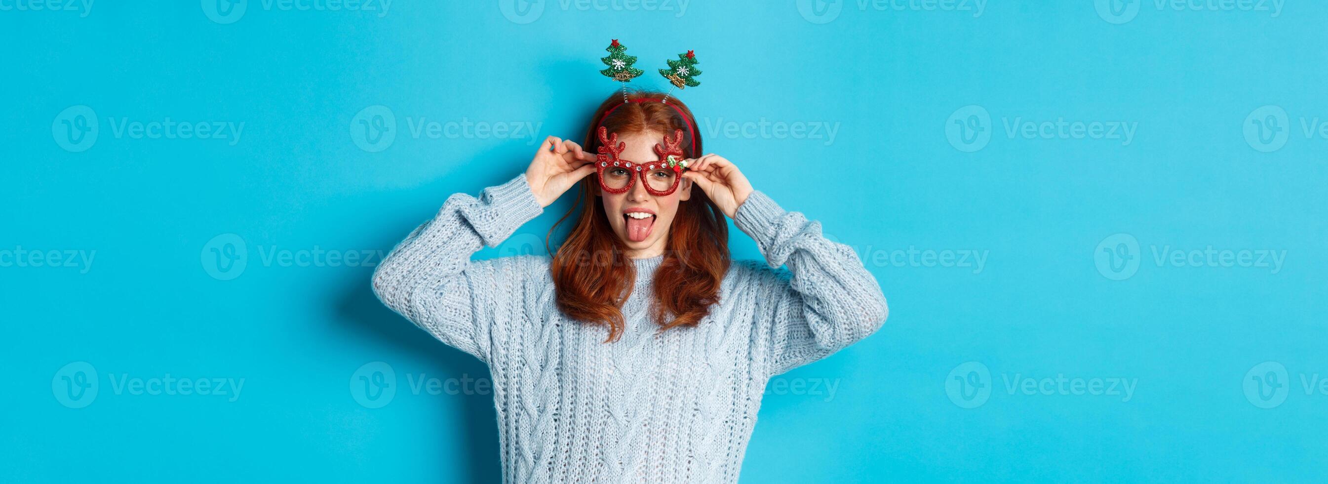 Winter holidays and Christmas sales concept. Beautiful redhead female model celebrating New Year, wearing funny party headband and glasses, smiling at camera photo