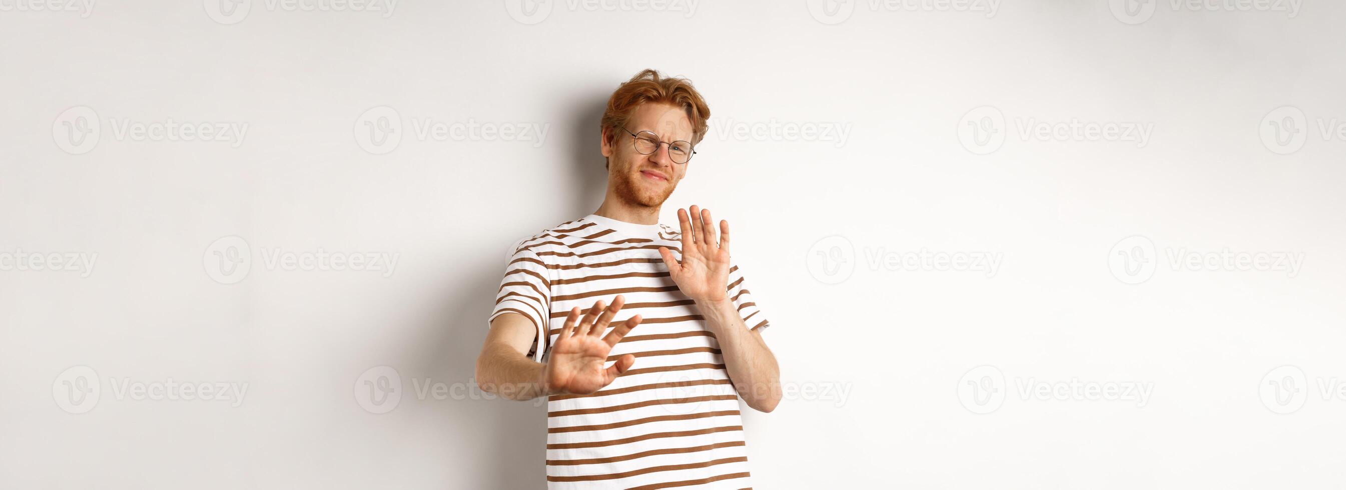 Displeased young man with red hair and bristle showing stop gesture, refusing something bad with disgusted face, standing over white background photo