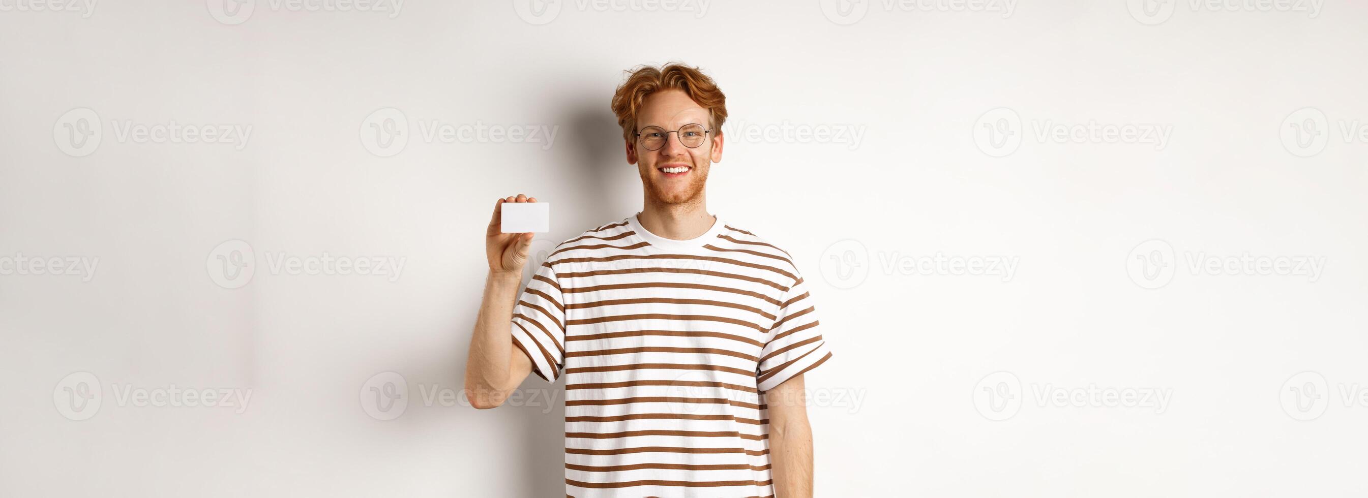 Shopping and finance concept. Smiling young man with bristle and red hair showing plastic credit card and looking happy, white background photo