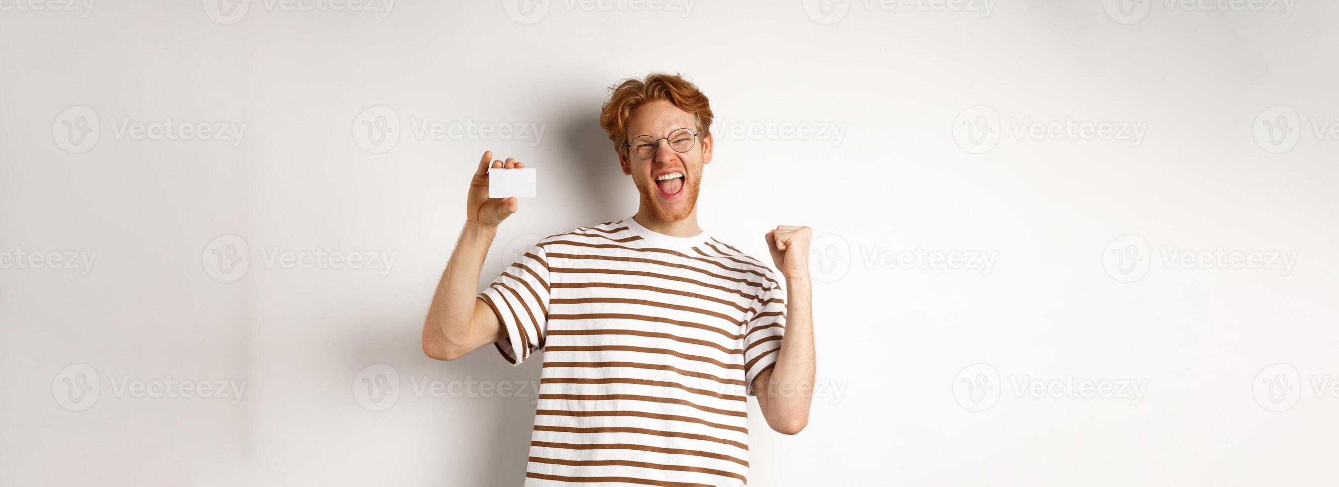 Shopping and finance concept. Young man winning bank prize, showing plastic credit card and making fist pump, screaming from joy and satisfaction, white background photo