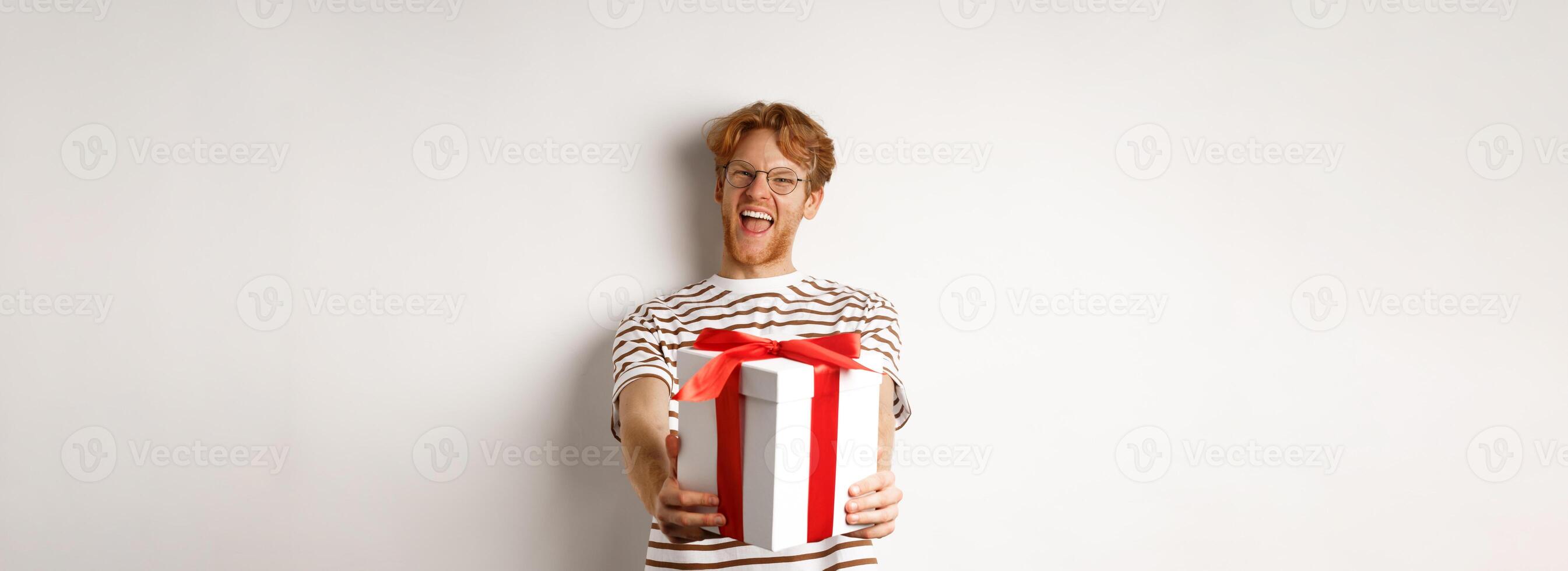 Valentines day and holidays concept. Happy redhead man smiling and giving you gift box, congratulating with birthday, standing over white background photo