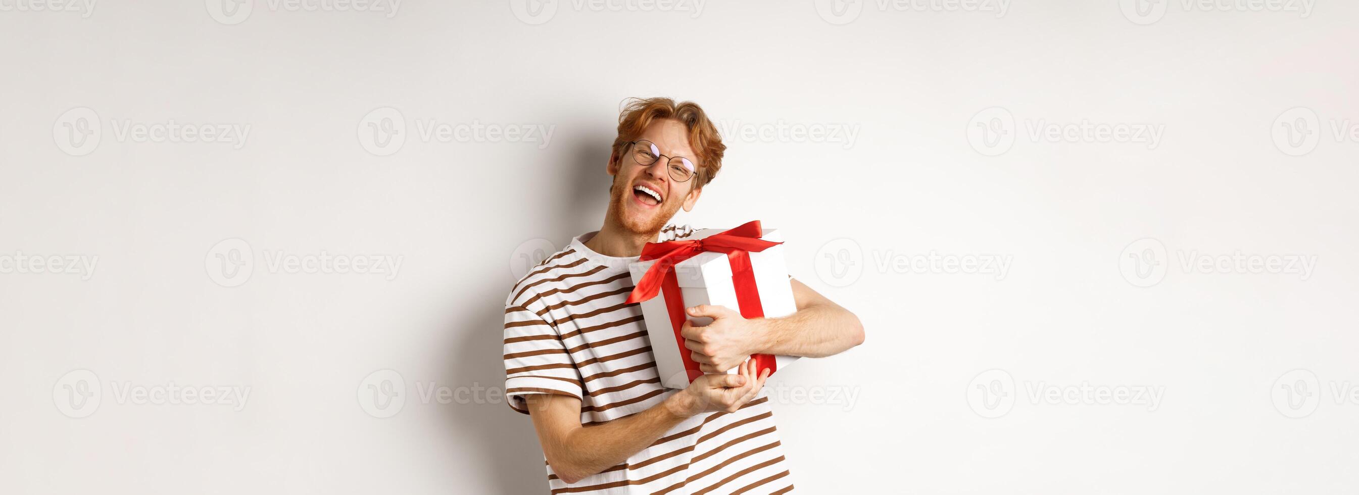 Valentines day and holidays concept. Happy redhead man hugging his gift box and thanking, looking at camera excited and grateful, white background photo