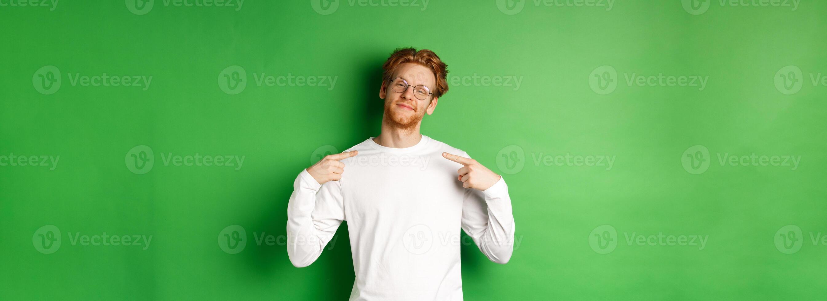 Confident and smug redhead man in glasses smiling, pointing at himself self-assured, standing over green background photo
