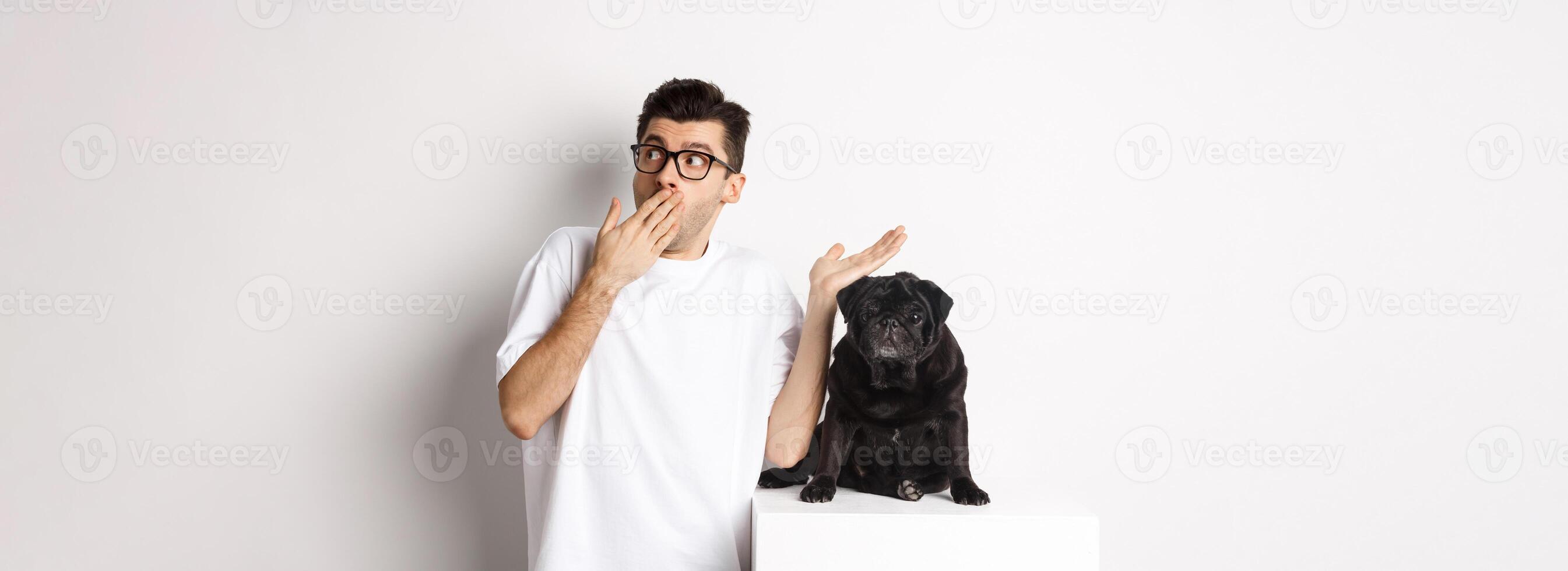 Surprised and shocked man in glasses, standing near cute black dog and staring right at logo, posing over white background photo